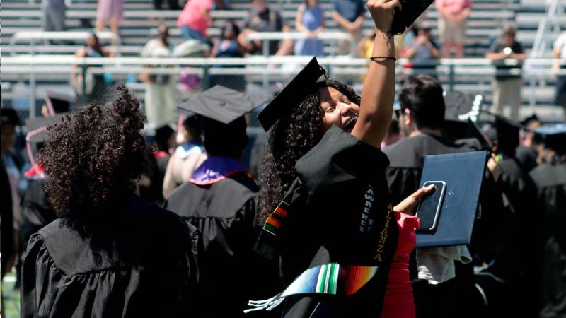Happy graduate holding degree in air during Commencement ceremony at Banta Bowl
