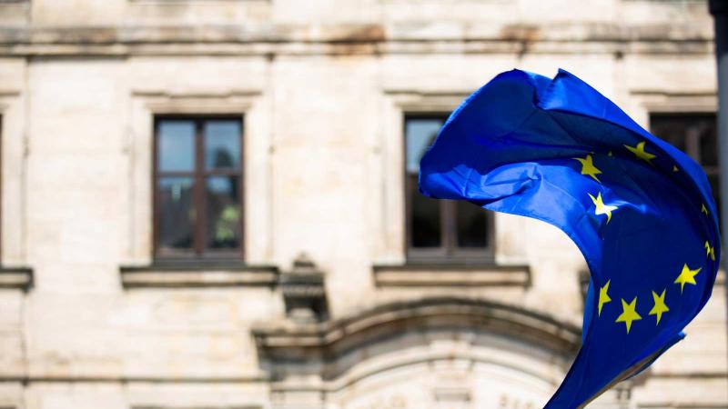 European Union flag waving in wind with concrete building in background