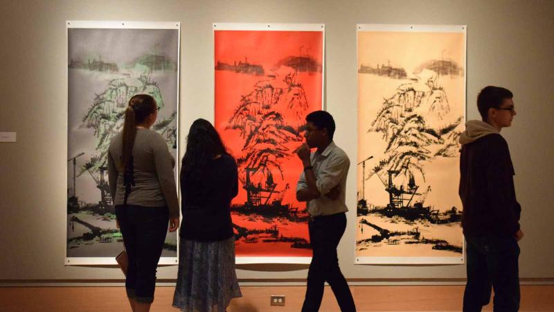 Image of four people looking at three art pieces on the wall
