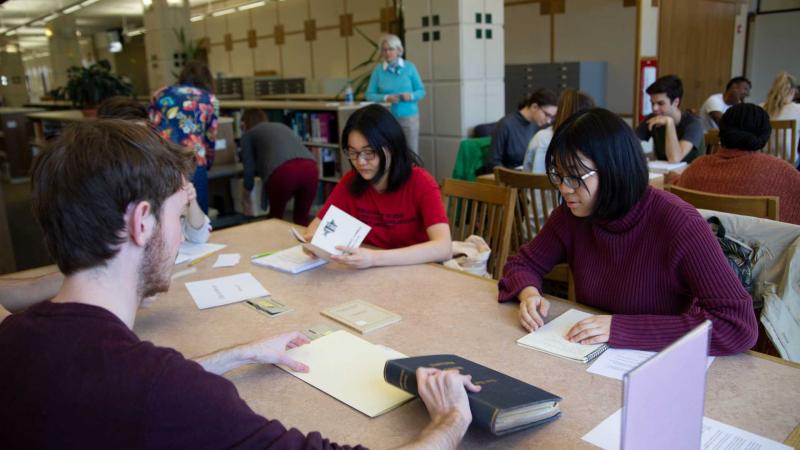 Group of students sitting at a table in the library looking at books and papers from the university archives.