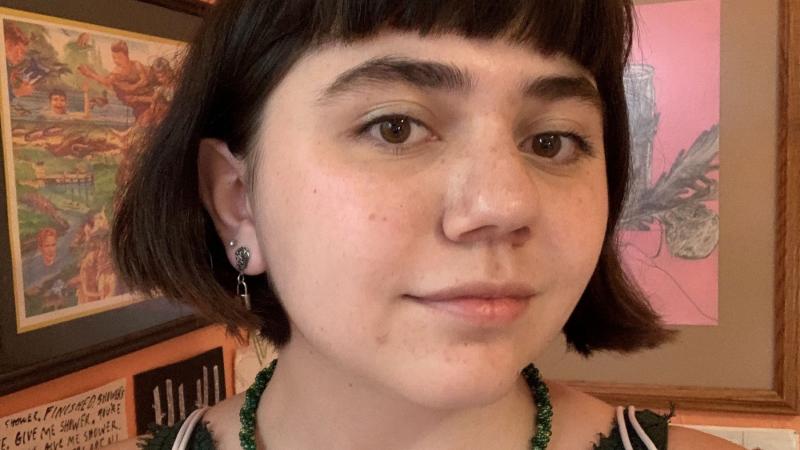 Emma Goodman, a student seeking an art degree from Lawrence, poses for profile pic in front of her art her art displayed on the wall in the background.