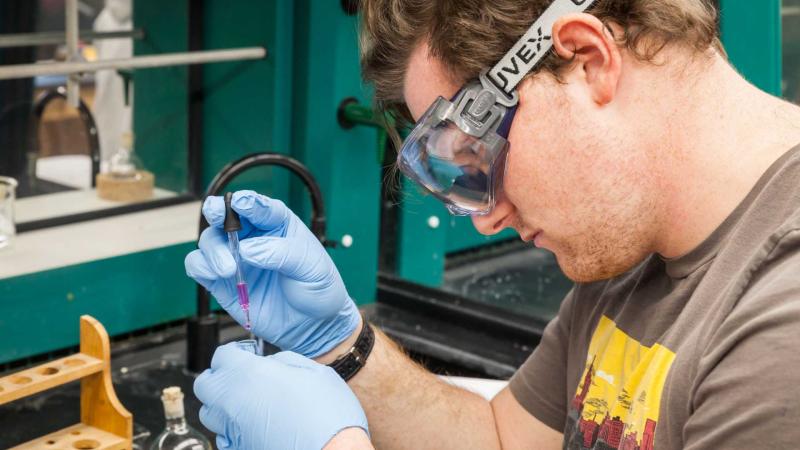 Student with safety goggles pipping purple liquid into test tube.