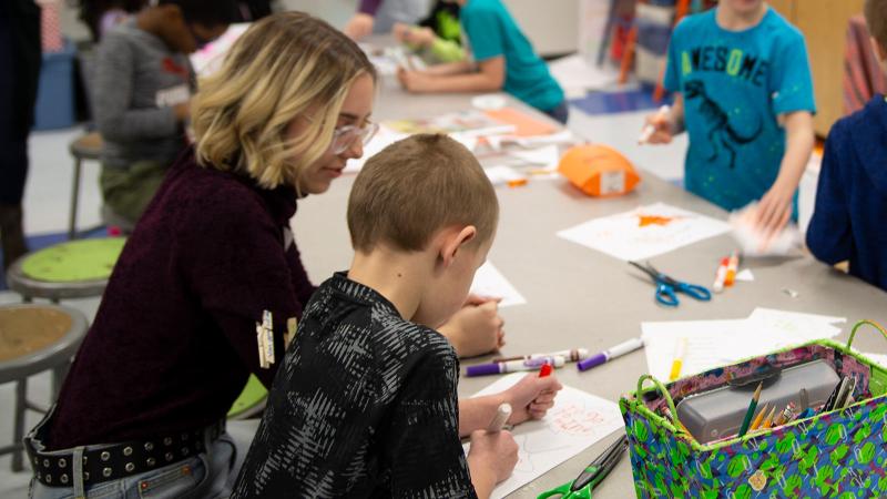 Students coloring with child at a school table