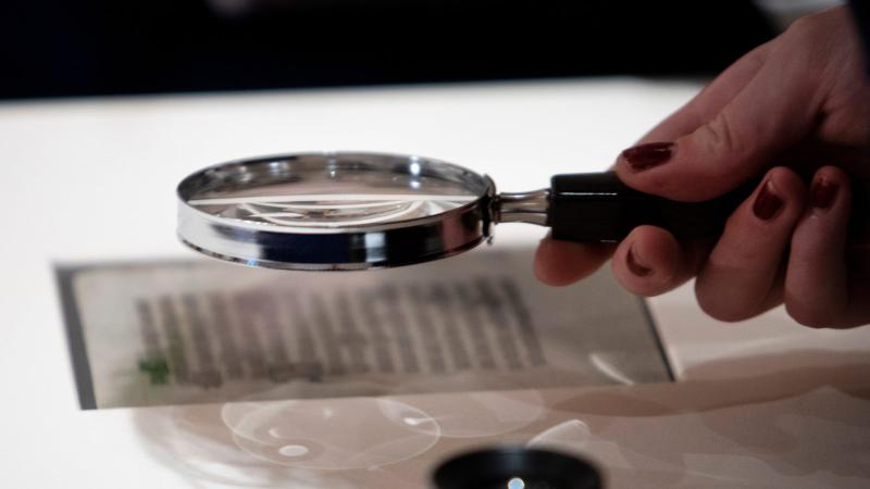 Hand holding a magnifying glass inspects parchment