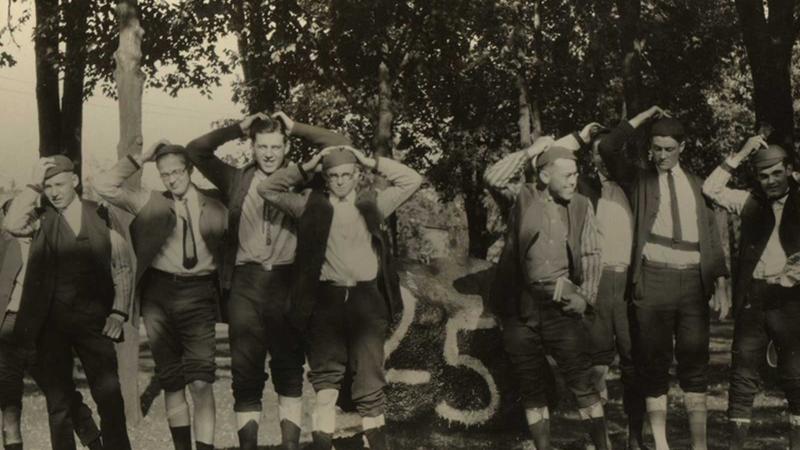 Men standing in a row holding both hands behind their head