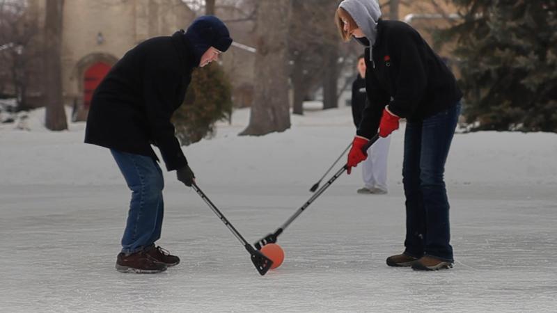 Two students with small brooms holding a ball during a broomball game 