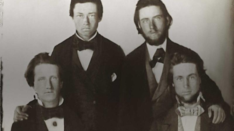 Four men posing for the camera, two are seated and two are standing