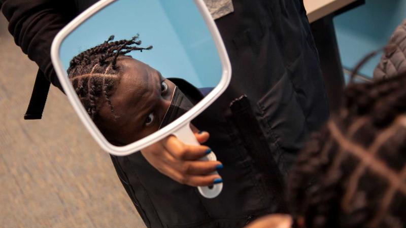 Eder Bellegarde looks up at a small mirror being held by Elle Tolan of Taperz Barber Shop. 