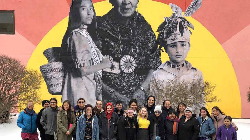 Native students stand in front of a colorful mural