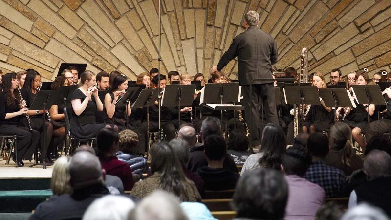 Wind ensemble performs on stage with people watching