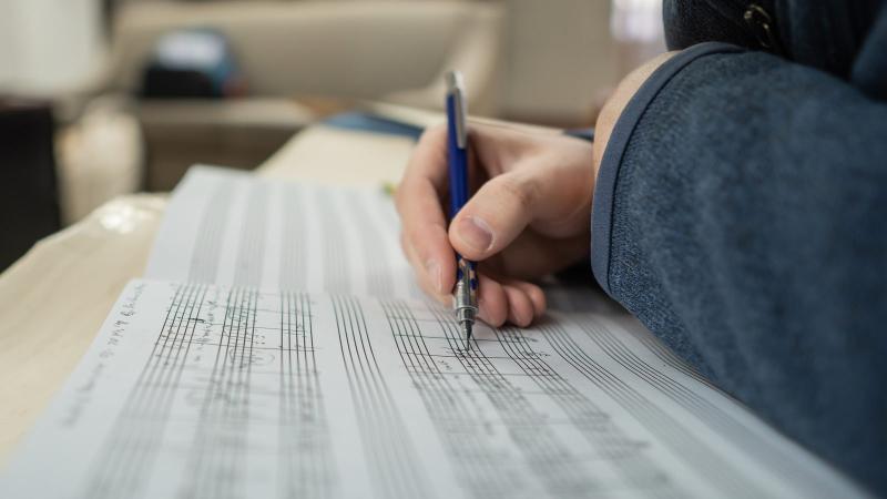 Hand holding pencil marking notations on sheet music
