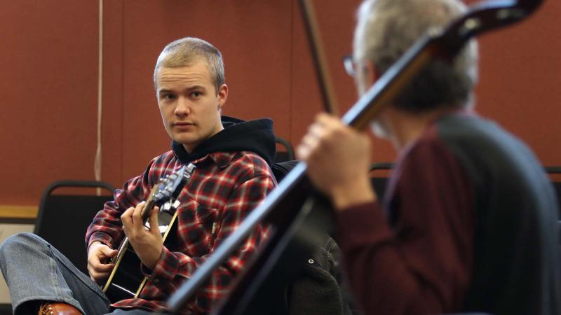 Student plays a guitar with faculty member