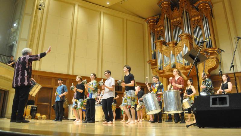 Large group of students, part of Lawrence University Percussion Ensemble, perform on stage. 