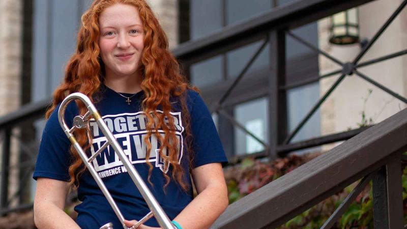 Mallory Meyer holding a saxophone in front of Alexander Gynasium