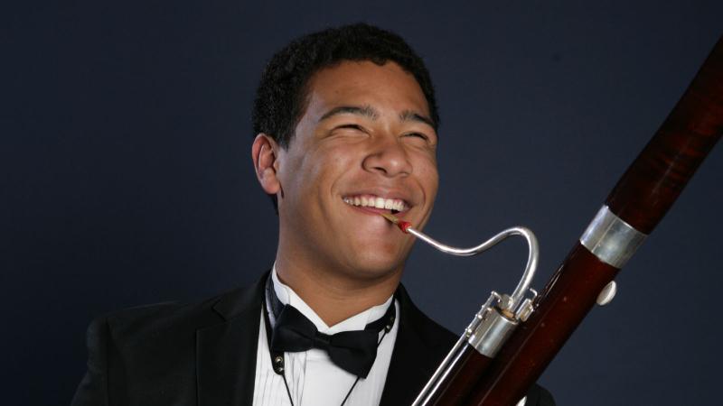 Nate Scott plays a bassoon while wearing a tuxedo and bowtie. 
