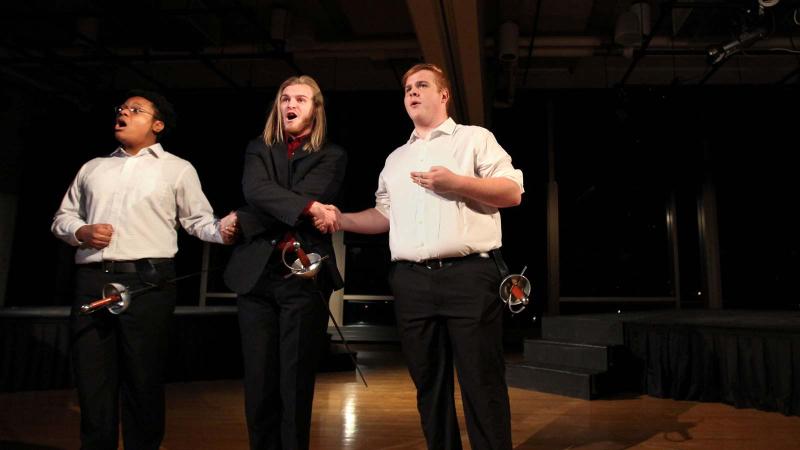 Three students rehearse on stage for an opera performance