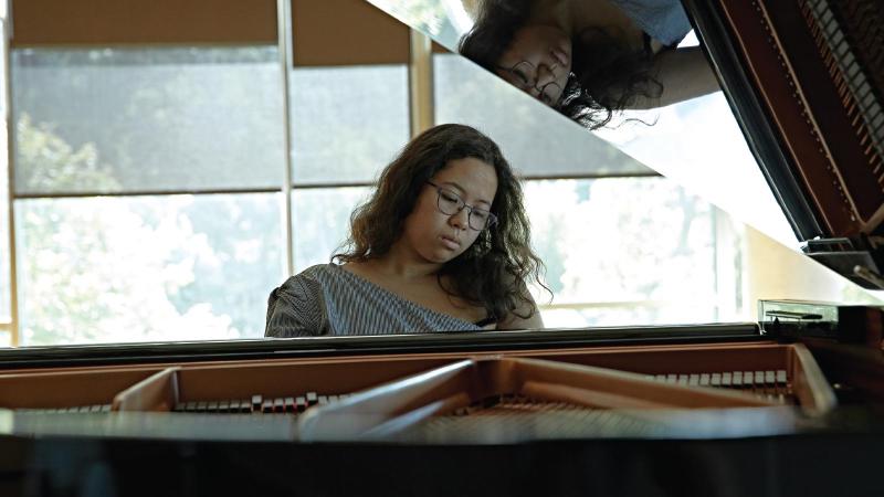 Student plays piano. Her reflection is shown on the piano.