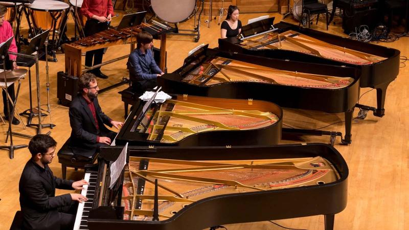 4 pianists playing pianos on stage