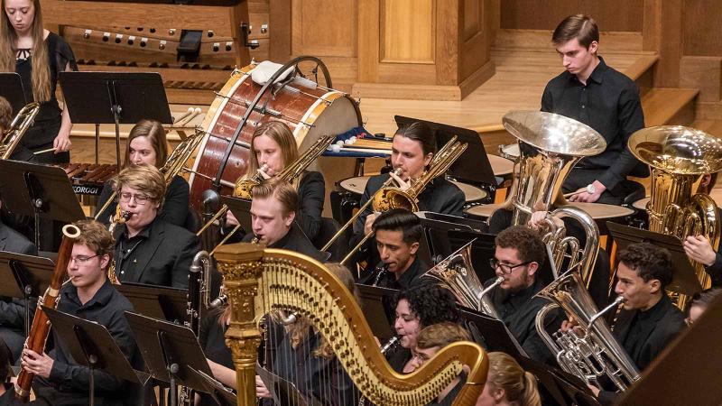 Many students playing band instruments on stage in Memorial Chapel