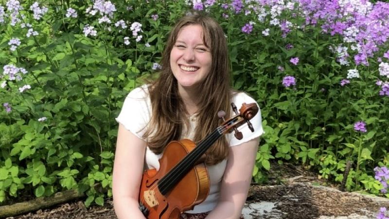 Mallory Welsch holds a viola in front of flowers.