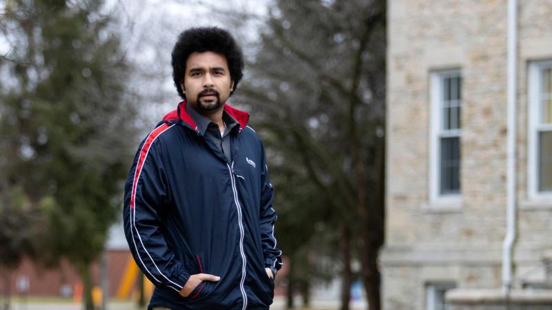 Abhishek Chakraborty, wearing a navy jacket, stands on Main Hall Green with his hands in his pockets.