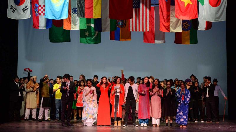 Entire cast of cabaret on stage under many international flags