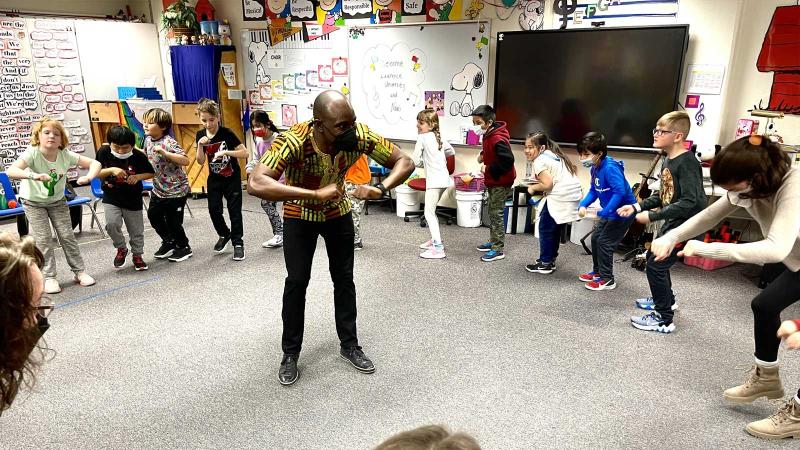 Student leading music class with lots of young students