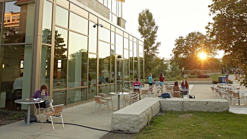 Students sitting at tables outside Warch Campus Center. Sun is setting.
