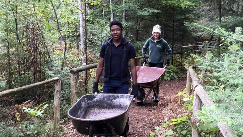 Students pushing wheelbarrows in forest