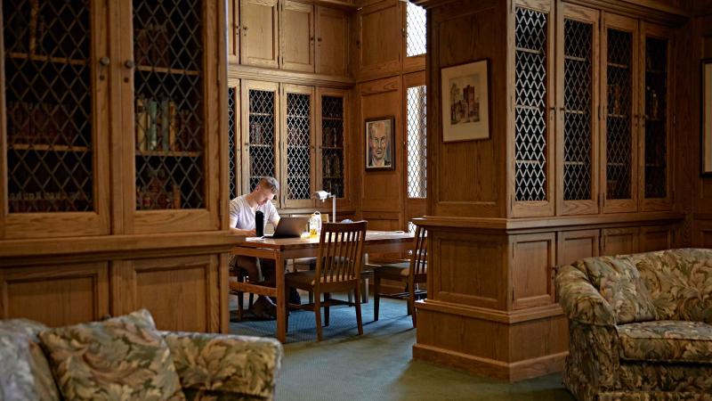 Student sitting a a table in the Milwaukee Downer Room, surrounded by wooden built-in bookshelves.