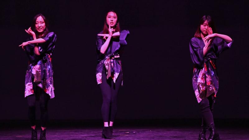 Three students dancing on stage with arms making a plus sign during 2022 Cabaret.