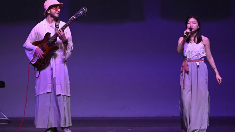 Student sings on stage while another plays the guitar