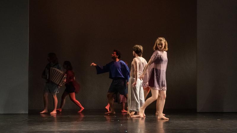 Six actors on dimly lit stage, frozen in mid-step