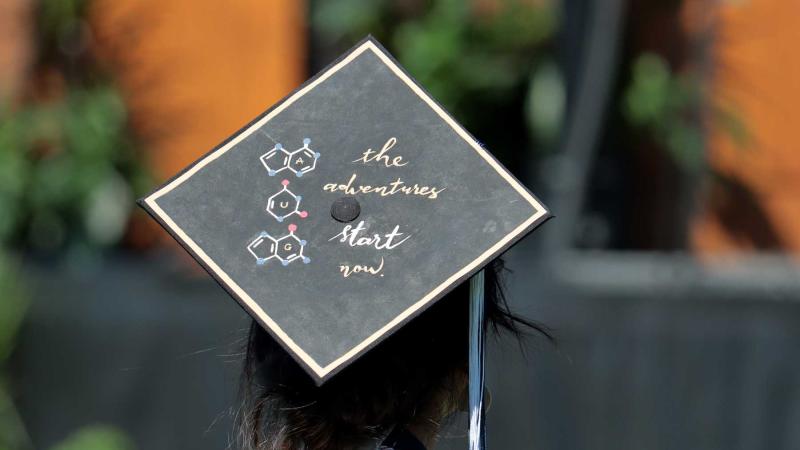 A commencement cap at the 2021 ceremony reads "the adventures begin now."