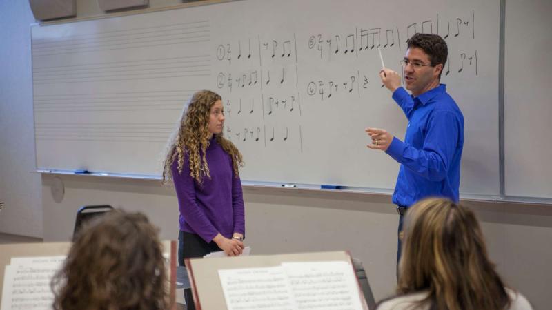 Student standing next to faculty by whiteboard with music notes on it.