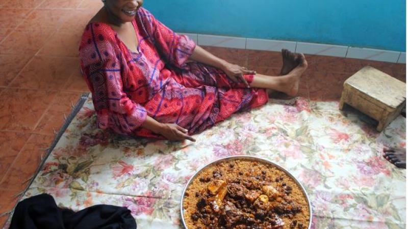 Senegalese woman sitting on blanket on floor in front of a shared bowl of food.