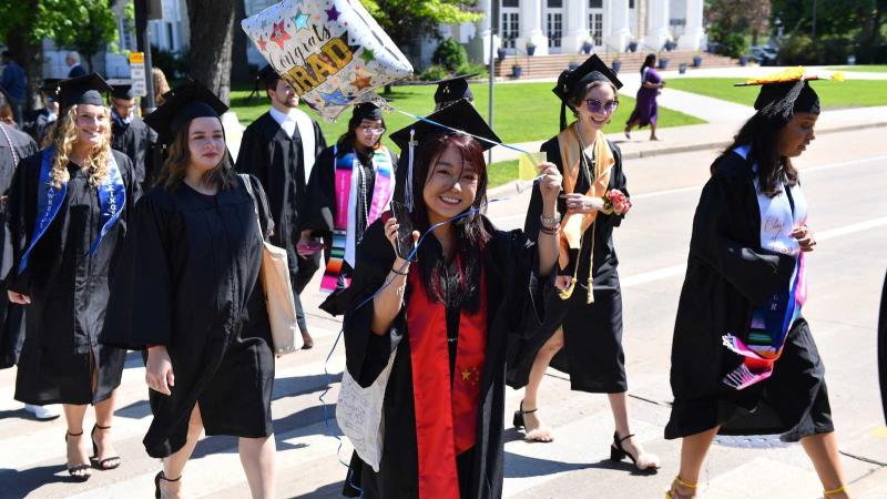 A graduate holds a Congrats Grad balloon as she and other graduates walk across College Avenue during the 2022 Commencement.