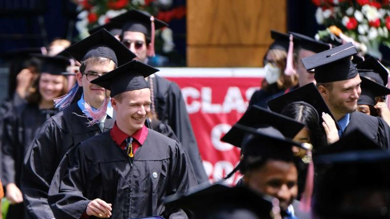 Graduates walk to the 2022 Commencement ceremony in their caps and gowns.