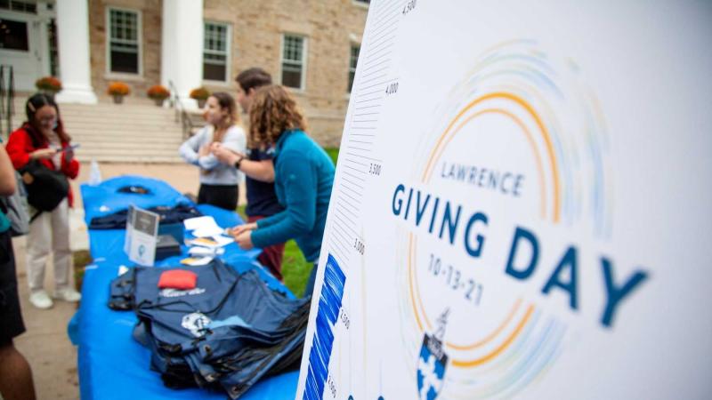 Students and staff give away t-shirts at a table on campus next to a Giving Day sign during 2021 Giving Day.