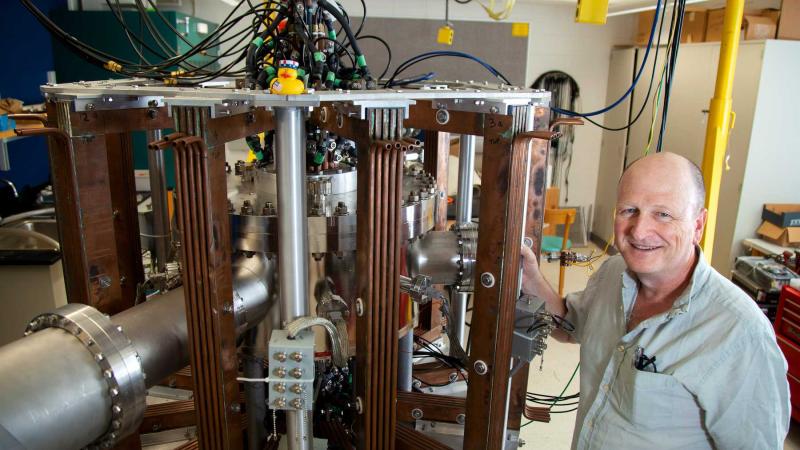 Physics professor Matthew Stoneking poses for a photo with research equipment in his lab in Youngchild Hall.
