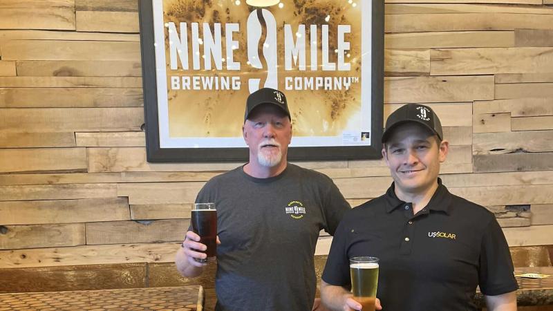 Bob Countryman and Ilan Klages-Mundt hold beers in front of a Nine Mile sign in their brewery.