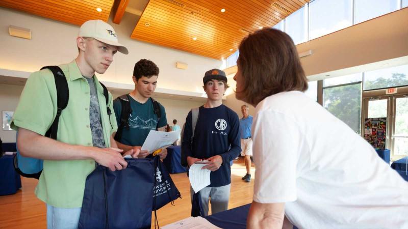 Henry Tibbetts-Zesbaugh, Ben Resnick, and Cormac Billick talk to a staff member at an information table during the Campus Resources Fair during New Student Move-in.