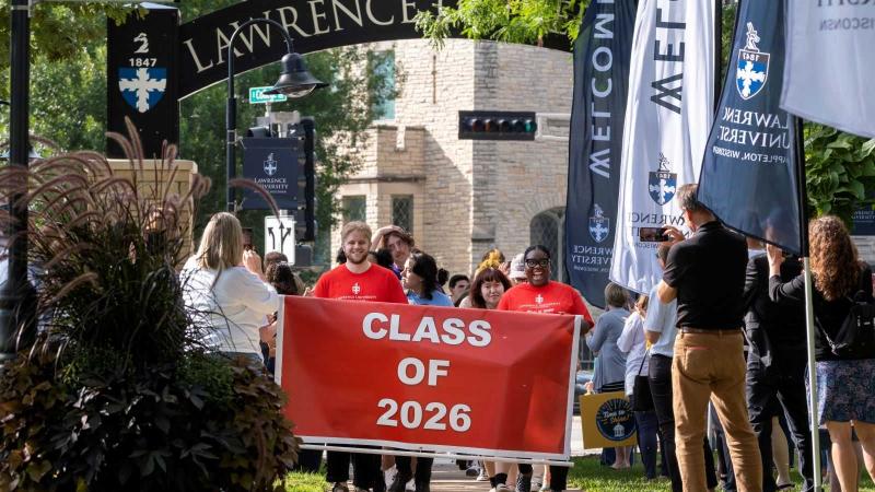 Incoming students carry the red Class of 2026 flag as they lead the processional under the arch.