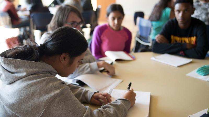 Summer Institute Participants sitting together at a round table, discussing and taking notes during class.