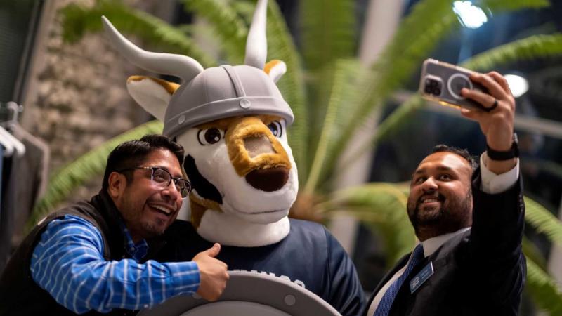Two alumni take photos with the new antelope mascot at a Friday night Homecoming gathering.