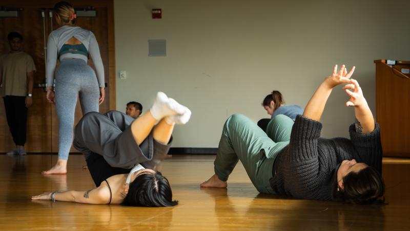 Students lay on floor with arms and legs in the air.