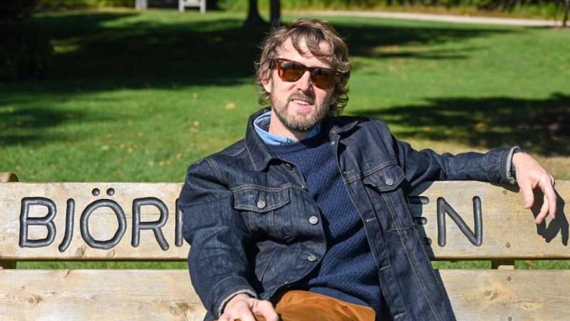 Tom McKenzie poses for a photo on a bench carved with the name Bjorklunden.