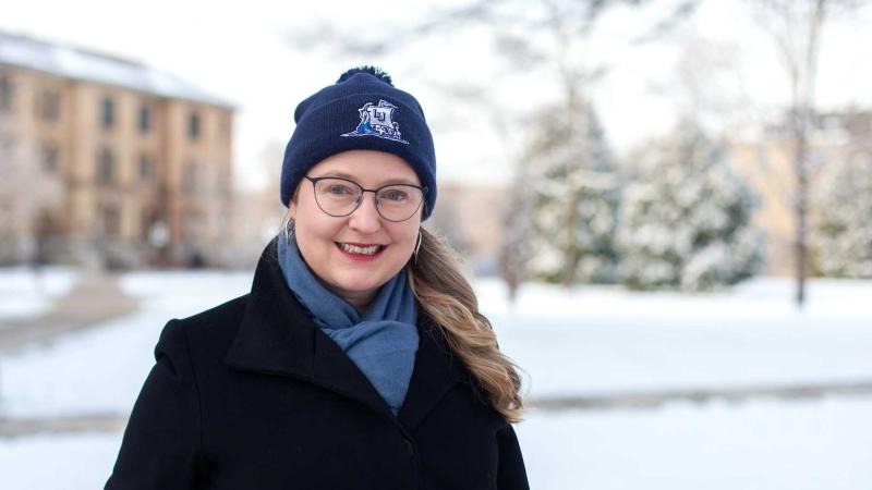 Nora Lewis wears a Lawrence winter cap and a black coat as she poses for a photo in the snow on Main Hall Green.