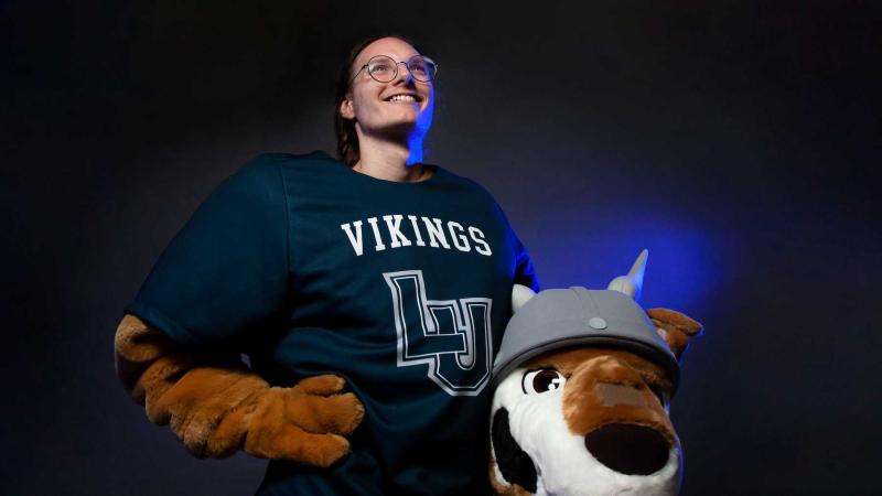 Spencer Brown poses for a photo bathed in blue light while holding the head of the Blu mascot.
