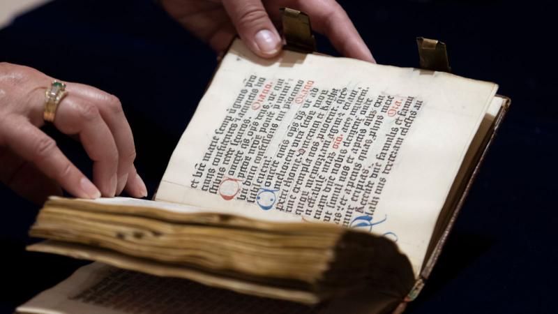 Hands holding an old text written using calligraphy